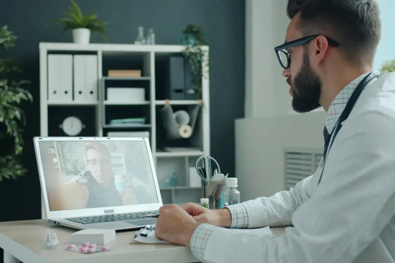 Arzt in der Praxis im Videogespräch mit einem Patienten am Laptop